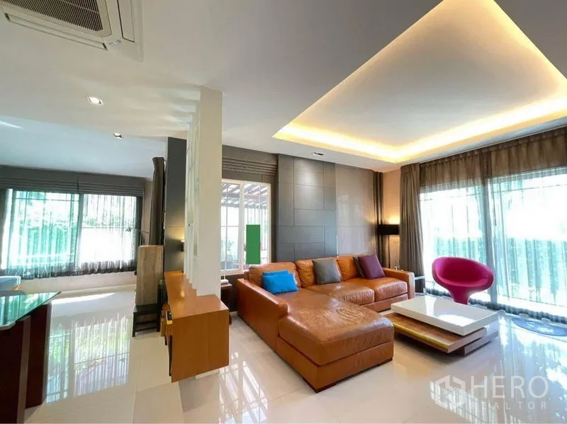 Detached House for sale in Prawet, Bangkok - Spacious living room with L-shaped leather sofa, large windows and recessed ceiling lighting.