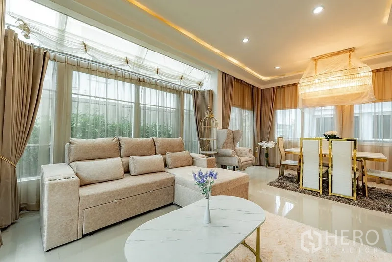 独立式住宅 出租或出售在Bang Khen, Bangkok - 客餐一体空间，环窗采光、米色沙发与造型吊灯。