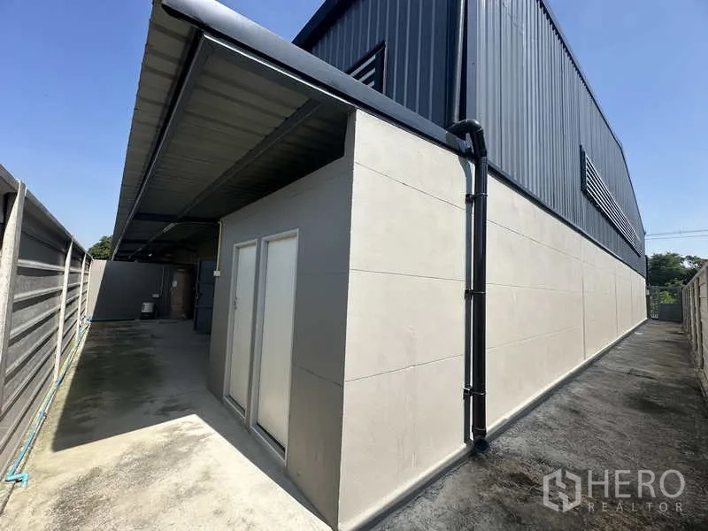 Warehouse for rent in Bang Bua Thong, Nonthaburi - Rear corridor with covered restrooms and reinforced boundary walls along the warehouse side.