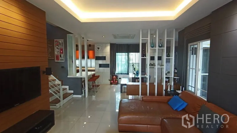 Detached House for sale in Prawet, Bangkok - Spacious living room with sectional leather sofa and open partitions to dining and stairs.