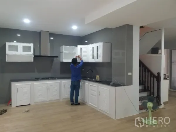 Townhouse for rent in Khlong Toei, Bangkok - Contemporary kitchen with white cabinets, range hood, black countertop and a gray backsplash wall.