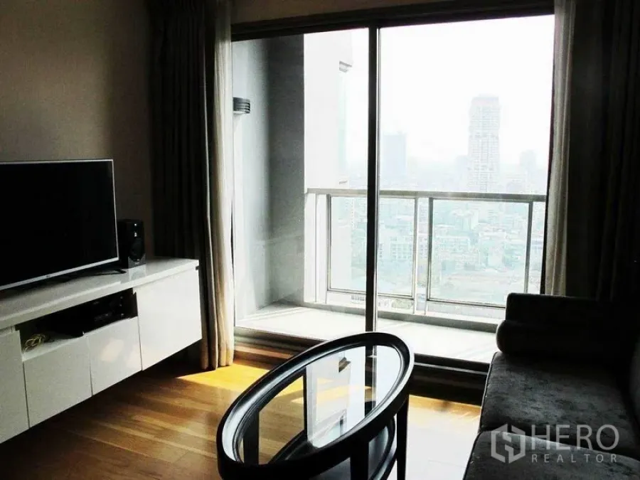 Condominium for rent or sale in Watthana, Bangkok - Living area opening to a balcony through sliding glass doors with city view.