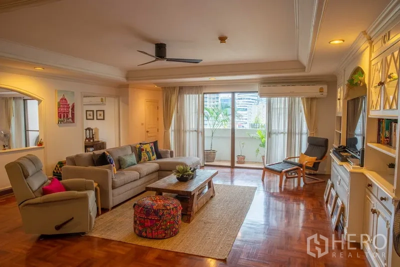 Condominium for rent in Khlong Toei, Bangkok - Bright living room with sofa set, built‑in shelving, sliding doors to a balcony and city views.