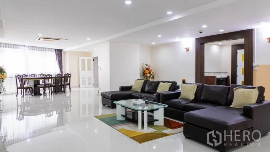 Condominium for rent or sale in Khlong Toei, Bangkok - Open-plan lounge and dining space with sectional sofas and large windows.
