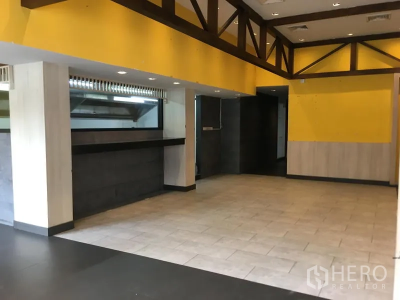 Retail Space for rent in Khlong Toei, Bangkok - Open-plan retail interior with yellow accent walls, exposed wood trusses, tiled floors, and a long service counter.