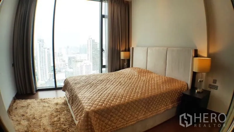 Condominium for rent in Khlong Toei, Bangkok - Master bedroom angle showing panoramic skyline through tall glass windows.