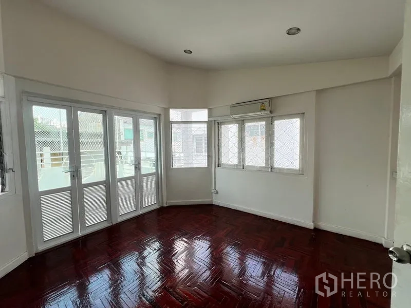 Home Office for rent in Watthana, Bangkok - Sunlit bedroom with balcony doors, air conditioning, and red parquet flooring.