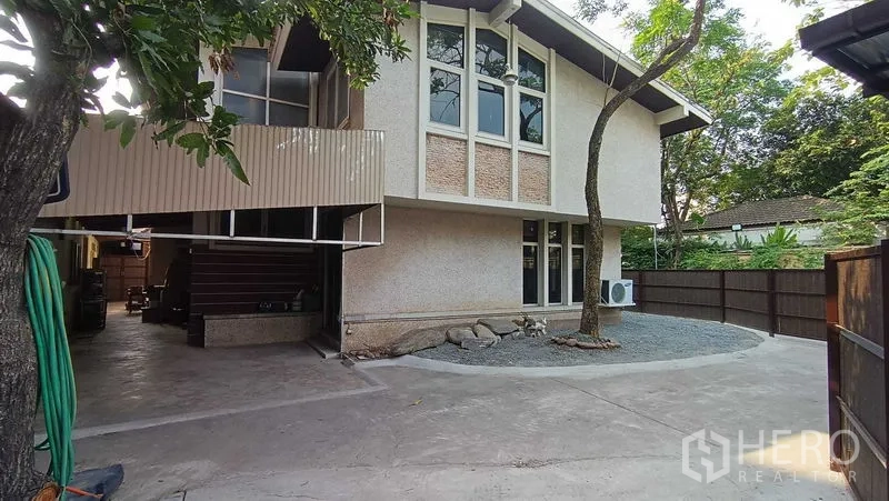 Detached House for rent in Phaya Thai, Bangkok - Side view of the house with gable roof, fenced yard, air-conditioning unit and spacious driveway.