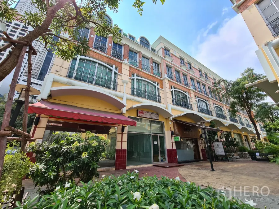 Shophouse for rent or sale in Sathon, Bangkok - Row of shophouses with brick-and-cream facade, arched canopies and ground-floor glass fronts along a landscaped walkway.