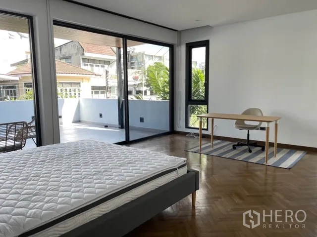 Detached House for rent in Watthana, Bangkok - Large bedroom with desk, rug, and access to an expansive terrace.