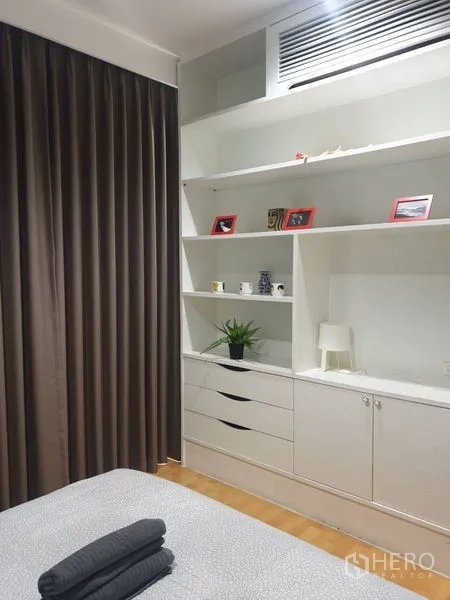 Condominium for rent in Khlong Toei, Bangkok - Bedroom corner featuring white built-in cabinets, drawers, and decorative shelving.