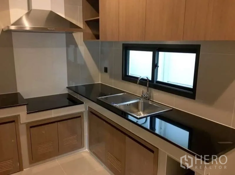 Detached House for rent in Bang Kapi, Bangkok - Modern closed kitchen with black stone countertops, double sink and range hood.