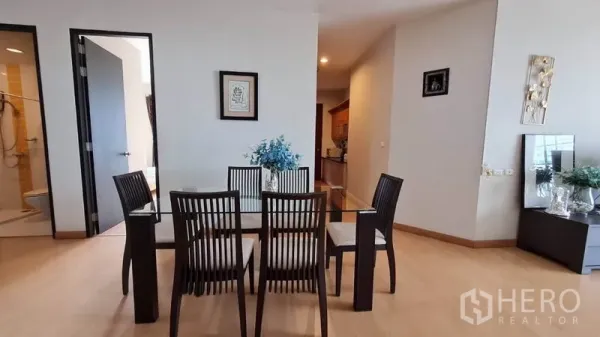 Condominium for rent in Khlong Toei, Bangkok - Dining area with a glass table and six chairs next to the hallway and bathroom access.