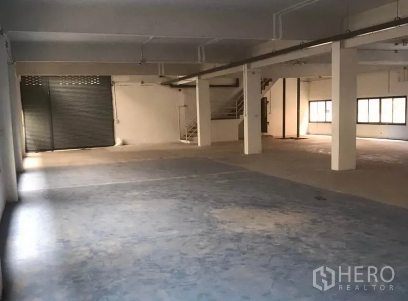 Factory for rent in Bang Bua Thong, Nonthaburi - Large ground-floor warehouse space with roller shutter door, concrete floor and support columns.