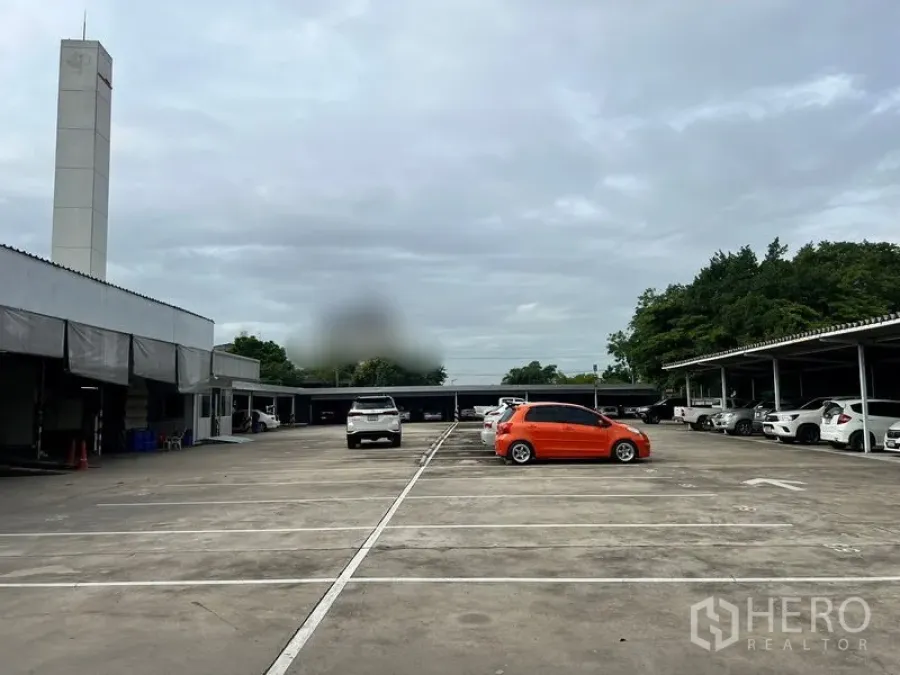 Land for rent in Bang Na, Bangkok - Central view of the large paved lot with carports on both sides and trees in the background.