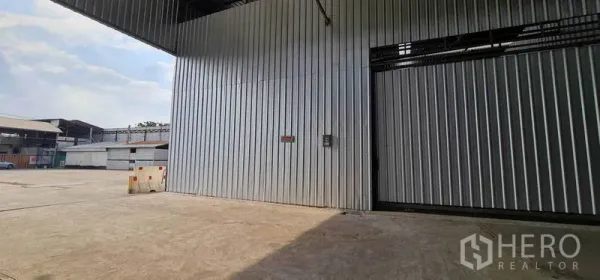 Warehouse for rent in Pak Kret, Nonthaburi - Warehouse exterior showing a wide concrete yard and covered loading area for trucks.