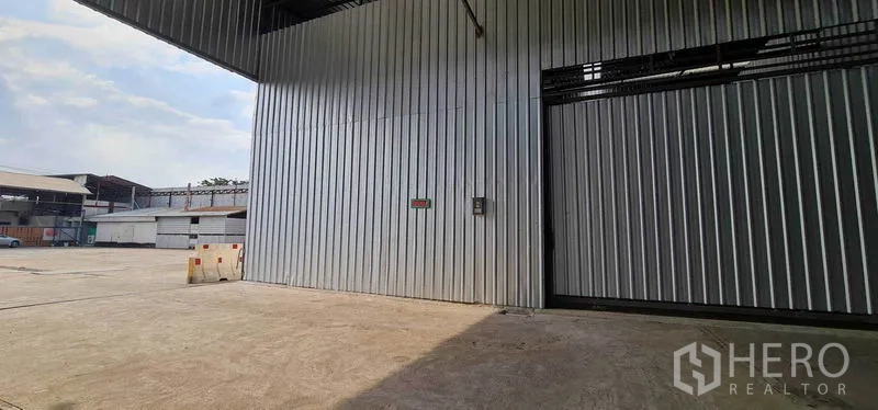 Warehouse for rent in Pak Kret, Nonthaburi - Warehouse exterior showing a wide concrete yard and covered loading area for trucks.