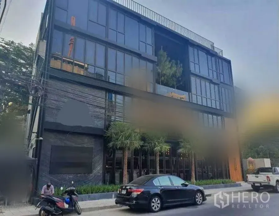 零售空间 出租在Watthana, Bangkok - 白天街景的现代低层商业建筑，椰子树与路边停车位