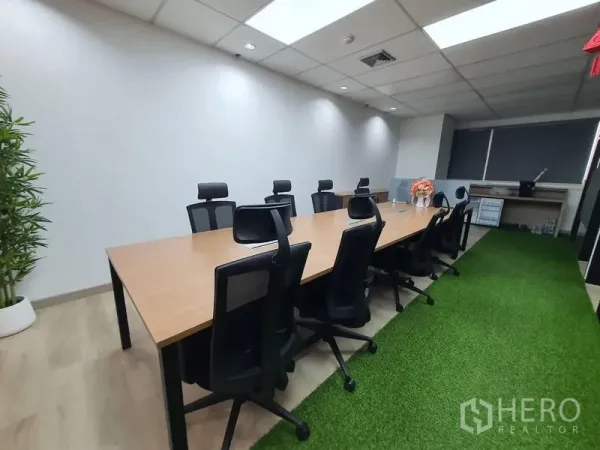 Office Space for rent - Bright boardroom with a long wooden conference table, ergonomic chairs and an artificial grass walkway.