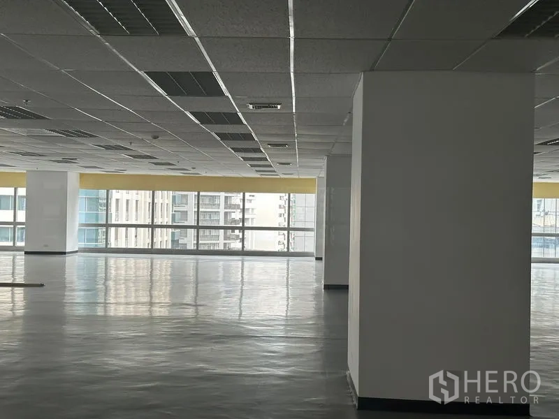 Office Space for rent - Bright corner of office floor with structural columns and full‑length windows overlooking nearby towers.