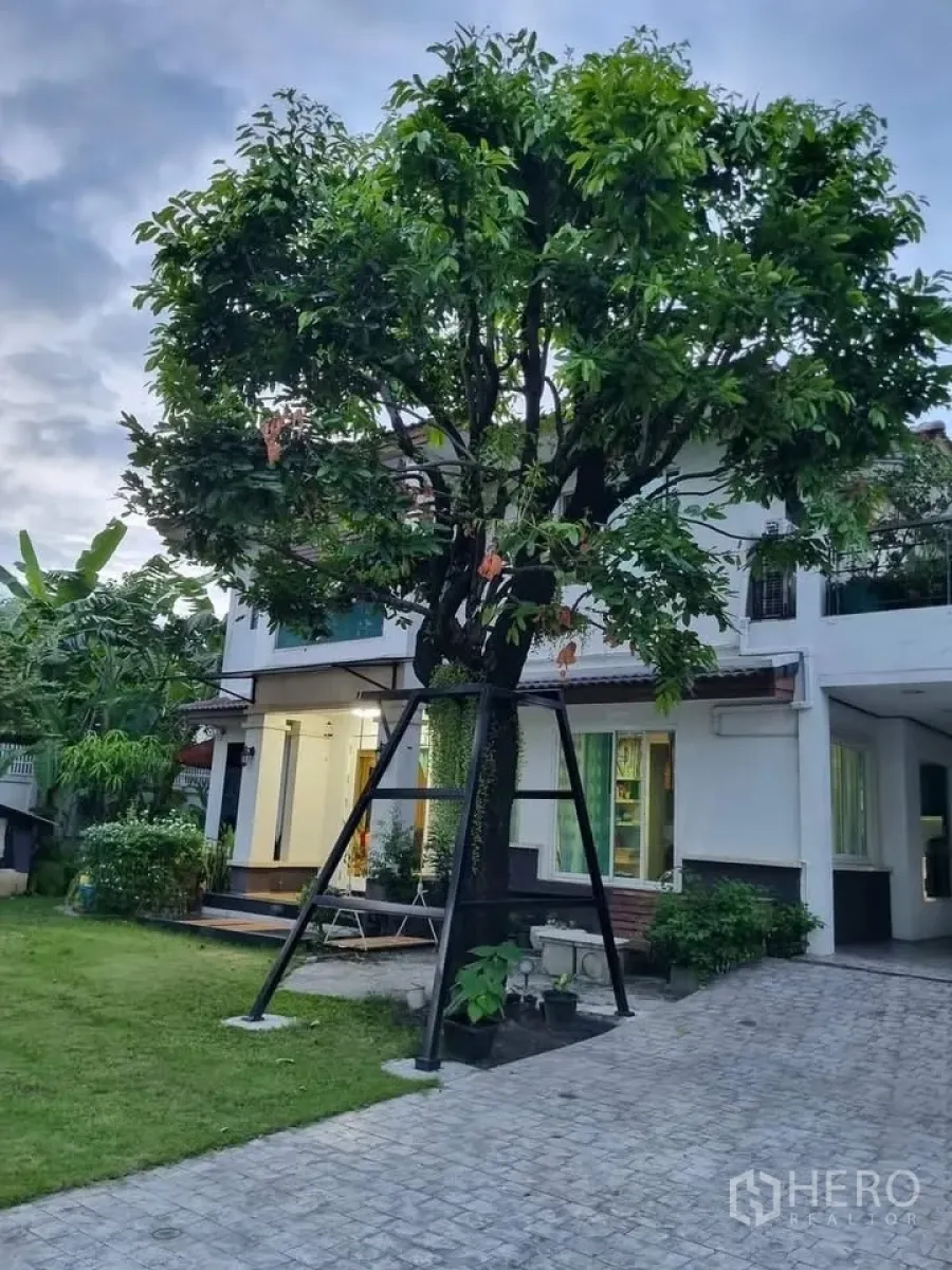 Detached House for rent in Bang Kapi, Bangkok - Two-storey detached house with large tree, lawn and lit porch at dusk.