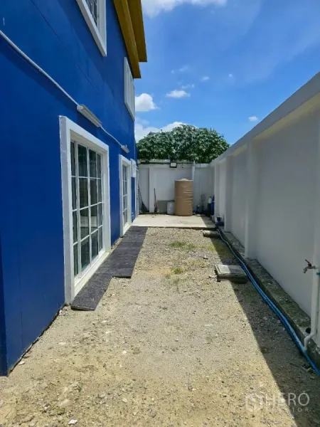 Warehouse for rent or sale in Khlong Toei, Bangkok - Side garden and service area with sliding glass doors and a water tank behind the building.