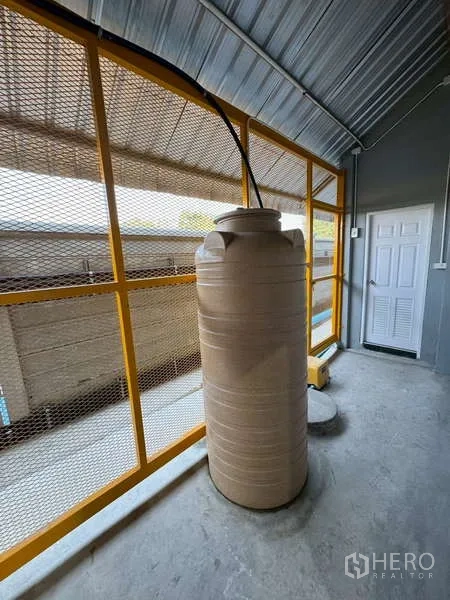Warehouse for rent in Bang Phli, Samut Prakan - Water storage tank under a metal roof next to a mesh wall and utility pump