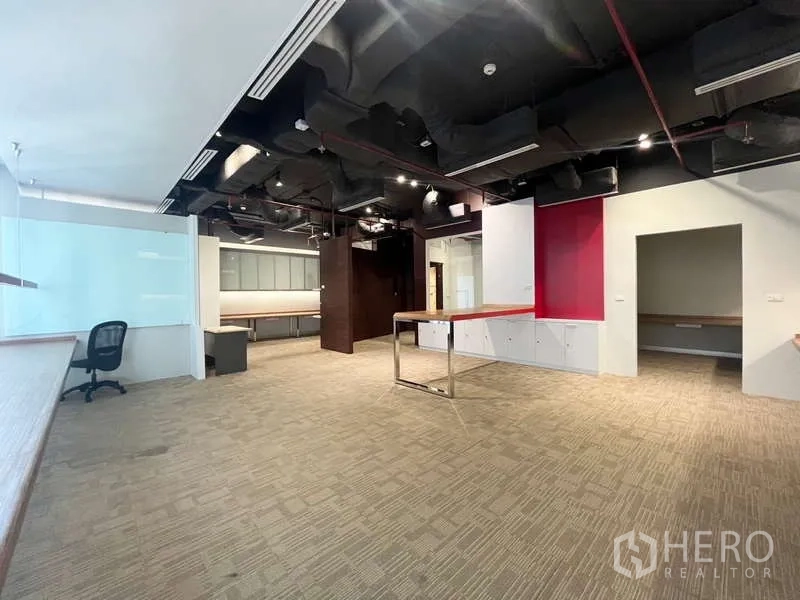 Office Space for rent in Watthana, Bangkok - Open-plan 117 sqm office with exposed black ceiling, carpet flooring, built-in counters and red accent wall.