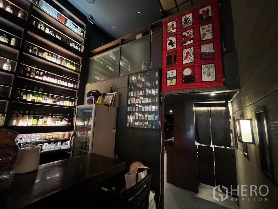 Shophouse for rent in Watthana, Bangkok - Close view of back bar shelves, a fridge and stairs to the mezzanine with red decorative wall art.