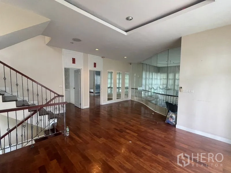 Detached House for rent or sale in Khan Na Yao, Bangkok - Upper-floor family area with polished wood floors, mirrored wall and staircase.