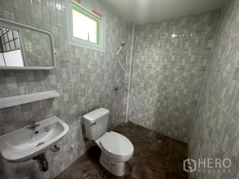 Warehouse for rent in Khlong Toei, Bangkok - Tiled bathroom with toilet, sink, mirror, small window, and handheld shower.