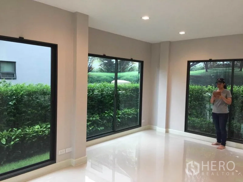 บ้าน ขายในPak Kret, Nonthaburi - ห้องนั่งเล่นสว่างด้วยหน้าต่างมุมกระจกขนาดใหญ่ มองสวน