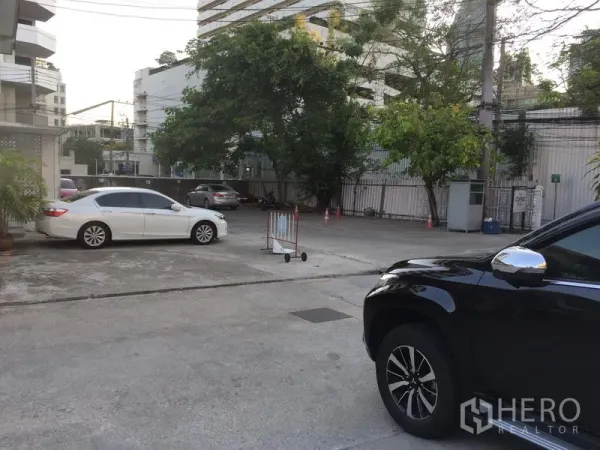 Retail Space for rent in Khlong Toei, Bangkok - Spacious courtyard-style car park with trees, entrance gate and surrounding condominium blocks.