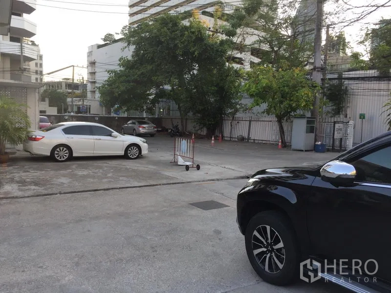 Retail Space for rent in Khlong Toei, Bangkok - Spacious courtyard-style car park with trees, entrance gate and surrounding condominium blocks.