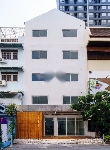 带办公室的家 出租在Khlong Toei, Bangkok - 四层白色住家办公楼，玻璃入口与木质装饰墙，周边为城市街景。
