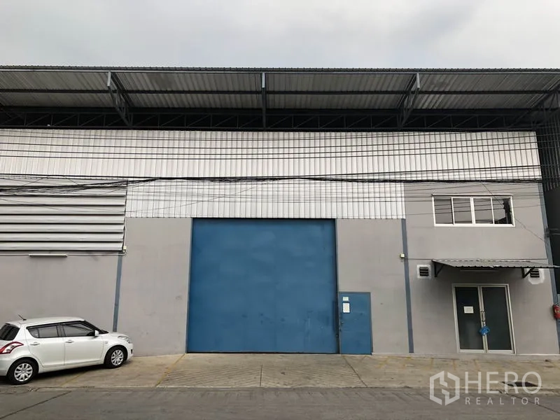 Warehouse for rent in Bang Kapi, Bangkok - Warehouse exterior in Bang Kapi, Bangkok with a large blue loading door and glazed office entrance under a canopy.