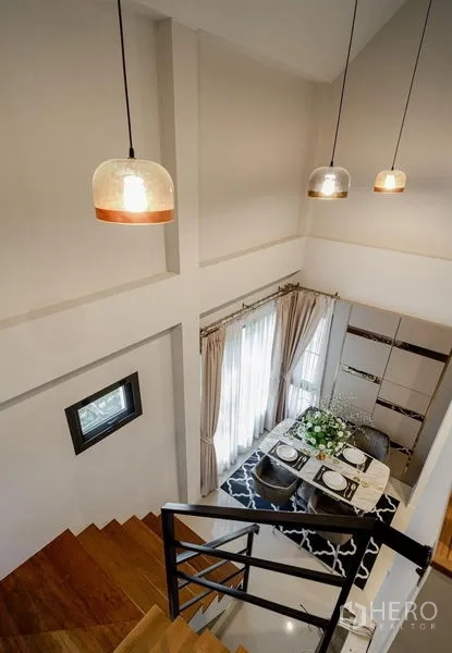 Detached House for sale in Lam Luk Ka, Pathum Thani - Staircase view over the dining area with pendant lights and tall windows.