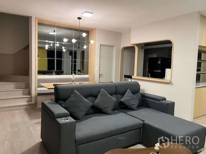 Detached House for rent in Prawet, Bangkok - Open-plan living room with sectional sofa facing dining area and kitchen hatch.