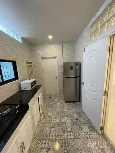 Townhouse for rent in Phra Khanong, Bangkok - Kitchen view showing window bars, refrigerator and microwave on the counter.
