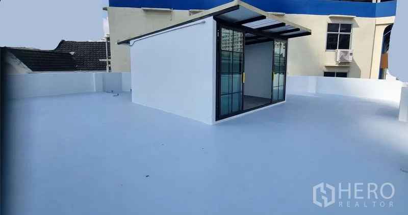 Shophouse for rent in Khlong Toei, Bangkok - Sunny rooftop terrace with a small glass entry pavilion overlooking neighboring buildings.