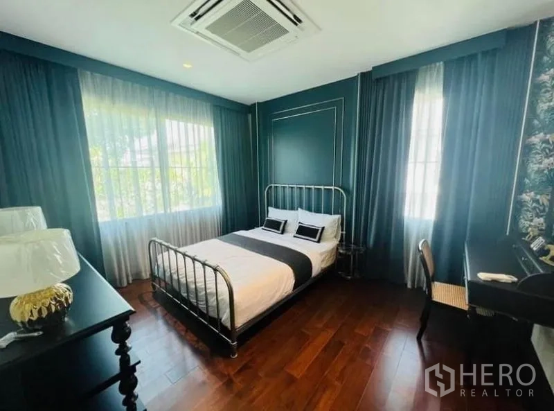 Detached House for rent or sale in Watthana, Bangkok - Bedroom with teal walls, metal frame bed and hardwood floors.