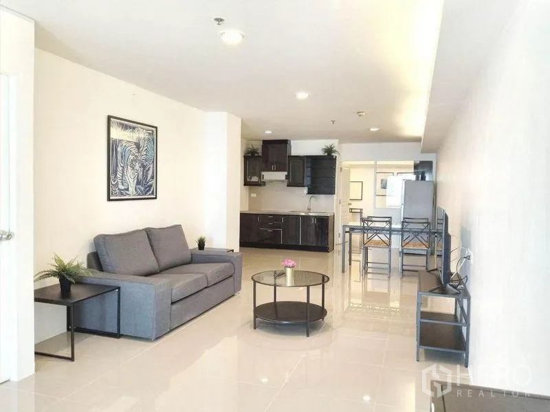 Condominium for rent in Khlong Toei, Bangkok - Bright open-plan lounge with grey sofa, coffee table, TV and kitchen in a Khlong Toei condo.