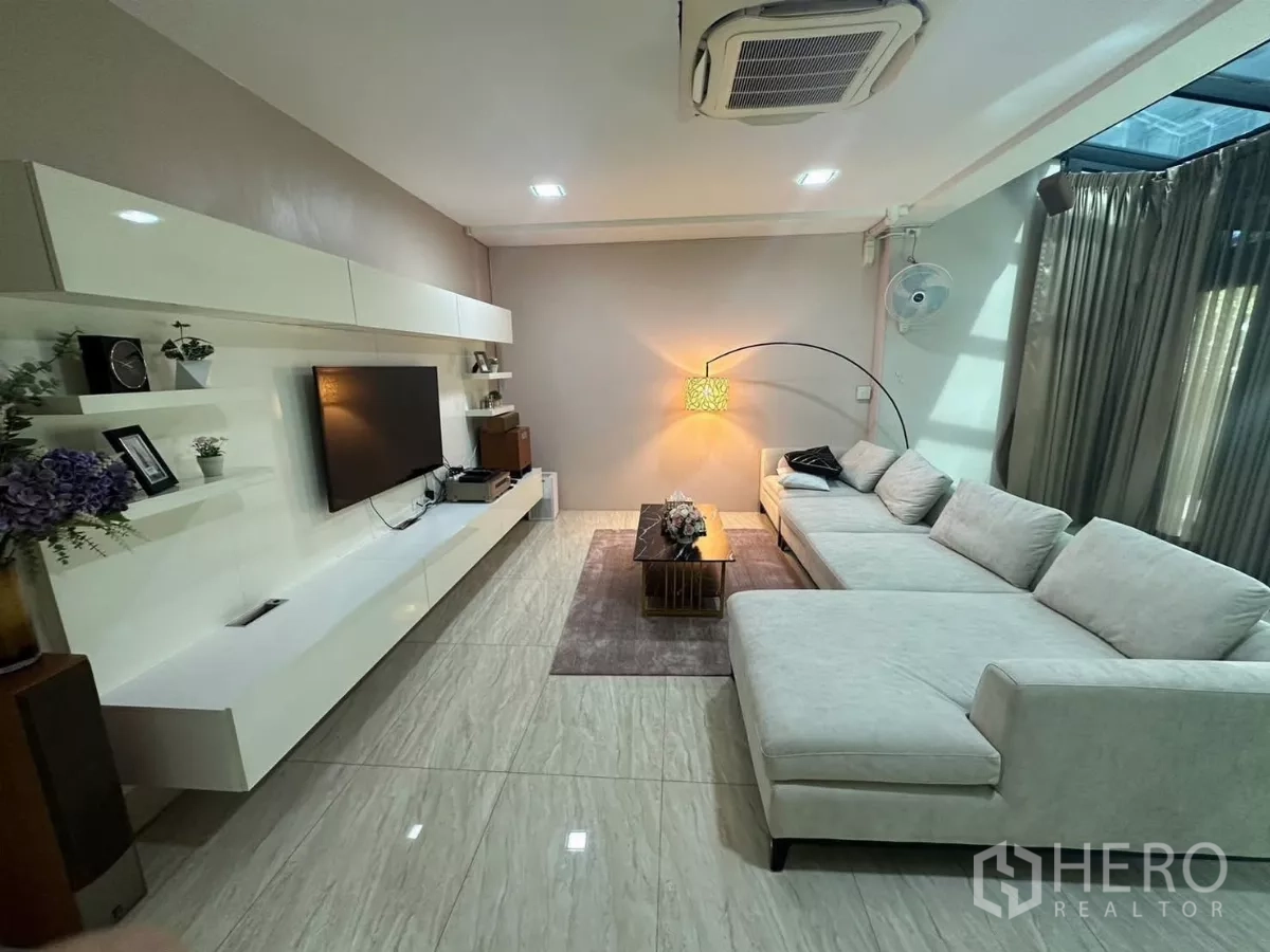 Detached House for rent or sale in Bang Kapi, Bangkok - Modern living room with L-shaped sofa, built-in TV wall and polished tile flooring.