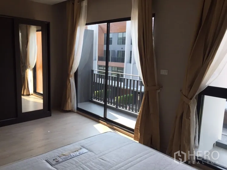 Townhouse for rent in Suan Luang, Bangkok - Primary bedroom with sliding glass doors opening to a balcony and a wardrobe.