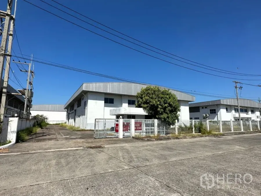工厂 出租在Chon Buri - 带围栏的大门工厂与宽阔车道，位于工业区，蓝天下清晰可见。