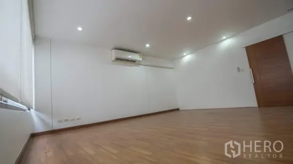 Townhouse for rent or sale in Phra Khanong, Bangkok - Spacious room with wood flooring, recessed lighting and a wall-mounted air conditioner.