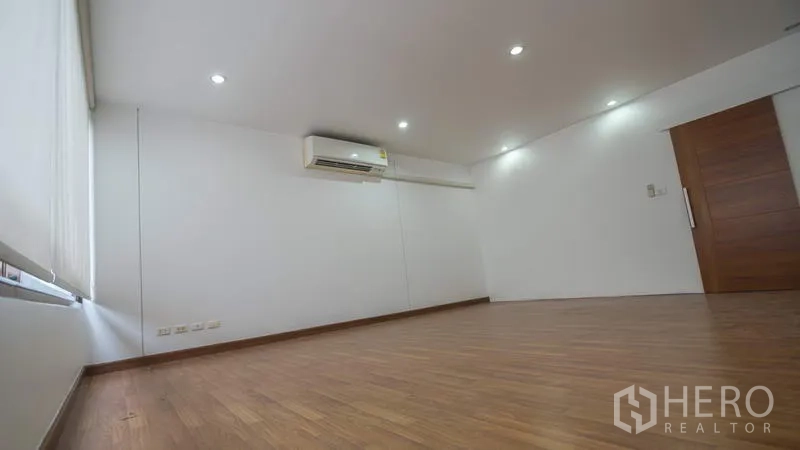 Townhouse for rent or sale in Phra Khanong, Bangkok - Spacious room with wood flooring, recessed lighting and a wall-mounted air conditioner.