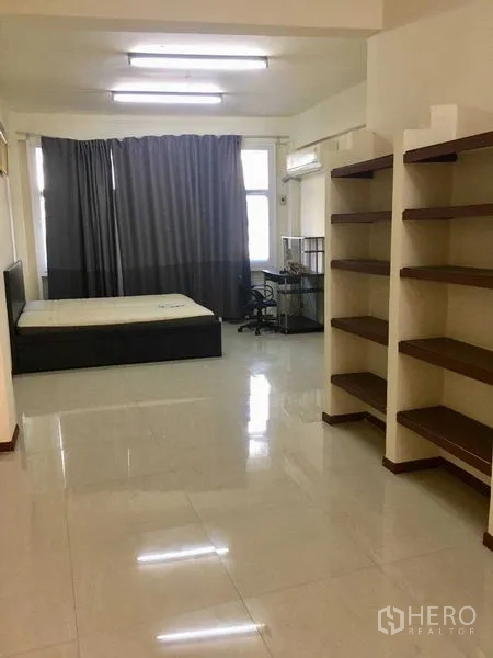Shophouse for rent in Suan Luang, Bangkok - Large studio-style room with tiled floor, wall shelves, bed, desk and air conditioner.
