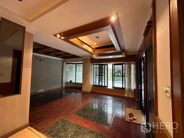 Townhouse for rent in Khlong Toei, Bangkok - Warm living room with coffered ceiling, large windows and mixed wood-and-stone flooring.