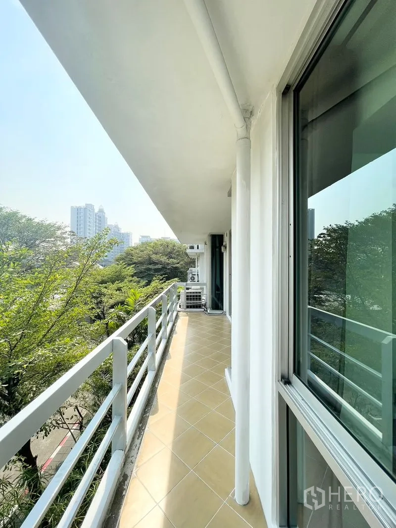 Condominium for rent in Khlong Toei, Bangkok - Long side balcony with railing and treetops beside sliding doors.